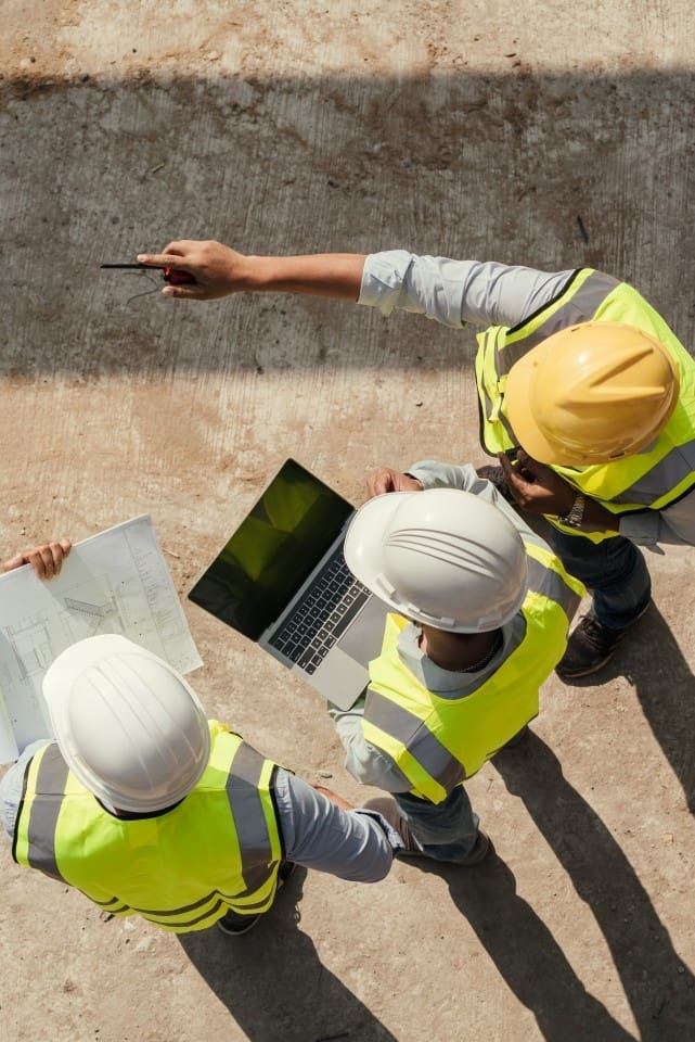 Vue de dessus : une équipe d’ingénieurs effectue une inspection de bâtiment à l’aide d’une tablette et de plans, sur un chantier de construction.