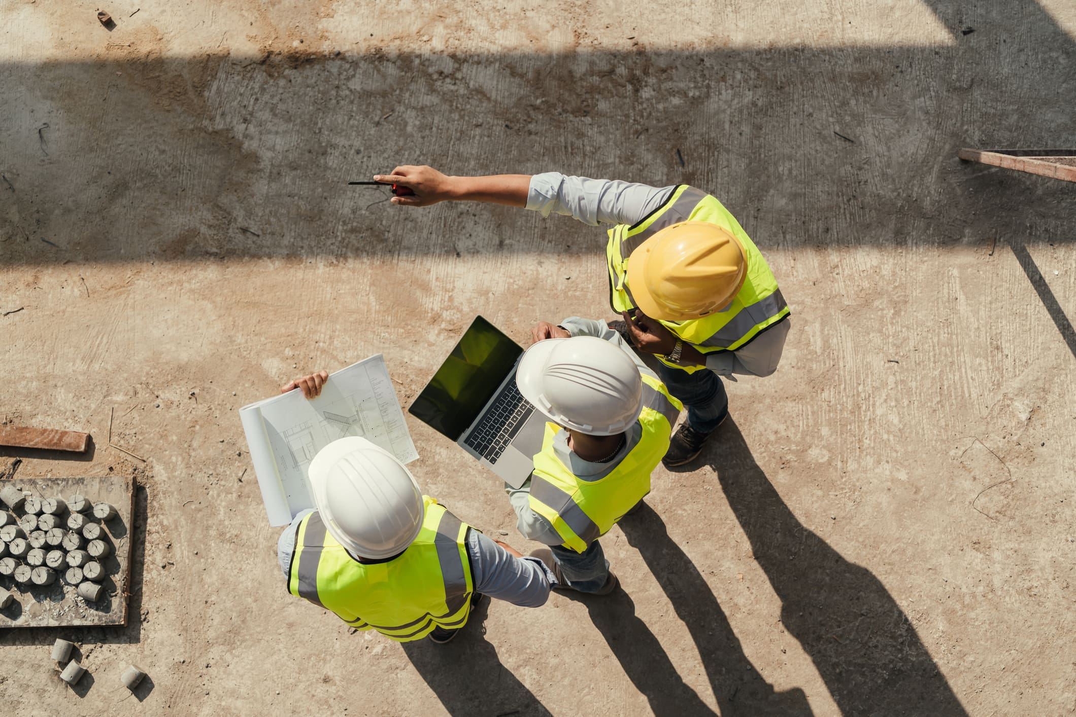 Vue de dessus : une équipe d’ingénieurs effectue une inspection de bâtiment à l’aide d’une tablette et de plans, sur un chantier de construction.
